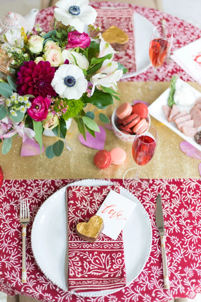 Romantische Tischdeko am Valentinstag gemusterte Decke in rot weiss kleines Herz in Goldgelb auf dem Teller viele Blumen in Vase
