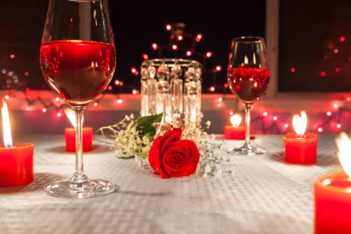 Romantische Tischdeko am Valentinstag weisse Tischdecke rote Teelichter rote Rose Weingläser roter Wein