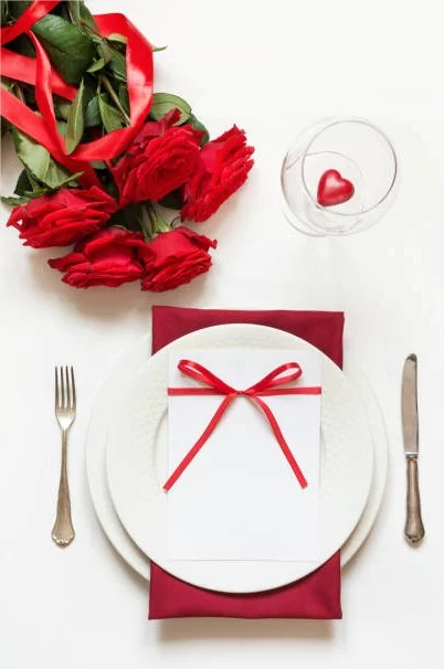 Romantische Tischdeko am Valentinstag weisse Tischdecke weisses Porzellangeschirr rote Schleife
