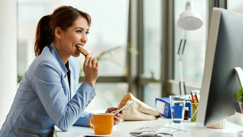 Young,Businesswoman,Using,Cell,Phone,While,Eating,A,Cookie,At